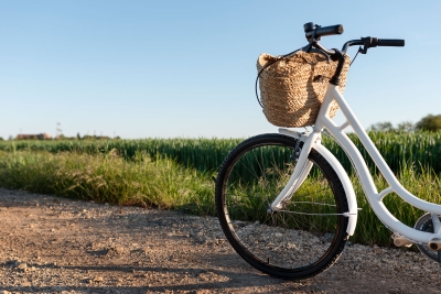 Weiße Fahrrad mit Korb am Lenker steht auf einem Schotterweg am Feldrand