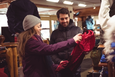 Zwei junge Menschen schauen sich im Bekleidungsgeschäft eine rote Jacke an.