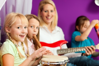 Kinder sitzen mit Musiklehrerin auf dem Boden und spielen auf Instrumenten Musik