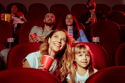 Mehrere Personen sitzen auf roten Kinosesseln und schauen gespannt und glücklich einen Film an