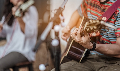 Ein Mann spielt Gitarre und im Hintergrund  spielt eine Frau Geige