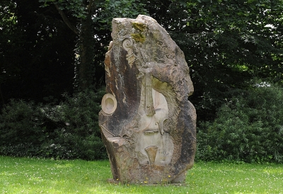 Sandsteinskulptur auf einer Wiese. Zu sehen ist eine Geige im Sandstein