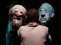 Theater Rückansicht eines Mannes der auf 2 große abstrakte Masken blickt.