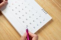 Kalender mit markierten Tagen Hand hält Kugelschreiber und zeigt auf ein Datum auf dem Kalender