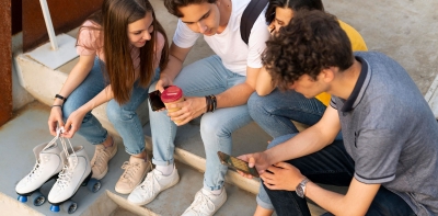 4 junge Erwachsene sitzen auf einer Treppe und schauen auf das Smartphone in den Terminkalender