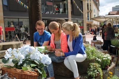 Eine Frau und ihre zwei Kinder sitzen bei Sonnenschein am Brunnen am oberen Markt in Ibbenbüren