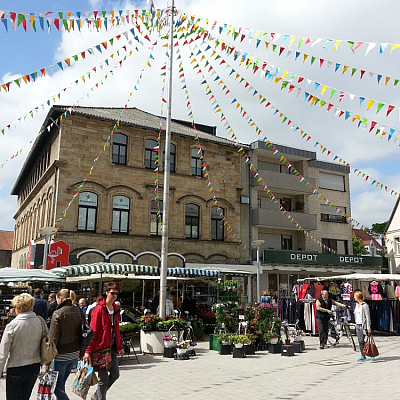 Oberer Markt in Ibbenbüren. Bunte Fähnchen hängen an einem Masten und Menschen machen einen Einkaufsbummel durch die Stadt