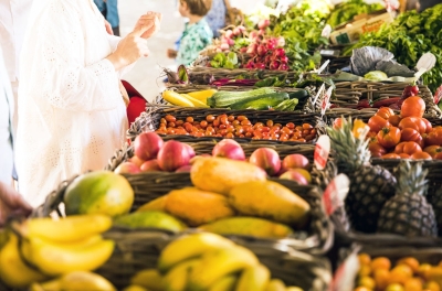 Frisches Obst und Gemüse in Körben und eine Frau bestellt etwas